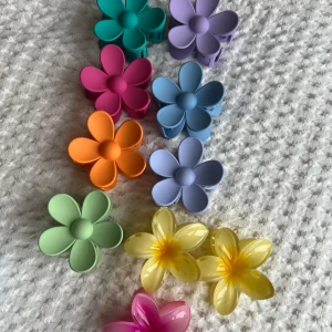 Färgglada hårklämmor i blommig design 2 st  - Säljer ett set med färgglada hårklämmor i form av blommor. Klämmorna kommer i olika färger: grön, orange, rosa, lila, blå och gul. Perfekta för att ge en färgglad touch till din frisyr. 