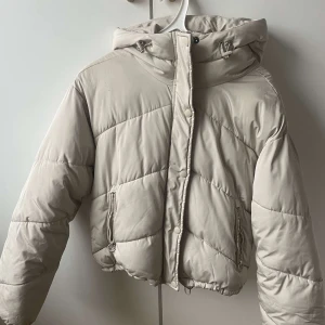 Beige pufferjacka från Pull&Bear - Säljer en snygg beige pufferjacka från Pull&Bear. Jackan har en quiltad design med dragkedja och knappar framtill. Den är försedd med en huva och har långa ärmar. Perfekt för kyliga dagar! Skriv om fler bilder eller frågor.🤗