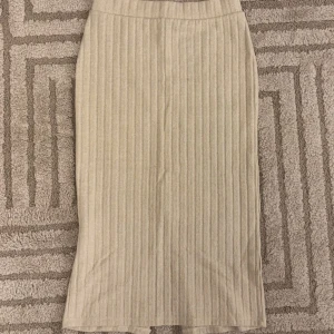 Beige ribbad kjol från Lindex - Snygg beige ribbad kjol från Lindex i en stilren design. Kjolen har en slits baktill som ger extra rörelsefrihet. Mycket bra skick storlek xs