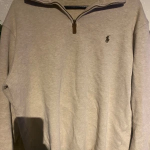Beige tröja från Polo Ralph Lauren - Säljer en stilren beige tröja från Polo Ralph Lauren med dragkedja vid halsen. Tröjan har en broderad logotyp på bröstet och långa ärmar. Perfekt för en avslappnad och snygg look.