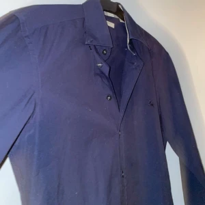 Mörkblå skjorta från Burberry Brit - Säljer en stilren mörkblå skjorta från Burberry Brit i storlek XS. Skjortan är tillverkad i bomull med en liten andel elastan för extra komfort. Den har långa ärmar och knappar framtill. Perfekt för en elegant look.