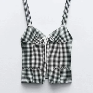 Svartvit rutig korsettopp - Trendig svartvit rutig korsettopp med knytning framtill. Den har breda axelband och en stilren design som passar perfekt för en chic look. Helt slutsåld från Zara och aldrig använd. Skriv för egna bilder