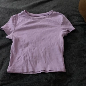 Lila ribbad topp från FSBN Sister - Säljer en söt lila ribbad topp från FSBN Sister i storlek XS. Toppen har korta ärmar och en rund halsringning, perfekt för en avslappnad stil. Tillverkad i Bangladesh.