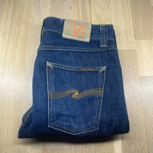 Mörkblå jeans från Nudie Jeans - Snygga mörkblå jeans från Nudie Jeans med klassisk femficksdesign och kontrastsömmar. De har en normal passform och är tillverkade i slitstarkt denim. Perfekta för en stilren look.