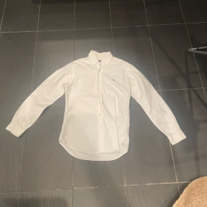 Vit skjorta från Ralph Lauren - Säljer en klassisk vit skjorta från Ralph Lauren i slim fit. Skjortan har långa ärmar och är dekorerad med det ikoniska broderade logotypen på bröstet. Perfekt för en stilren look. Skickar även paketet inom 24 timmar.