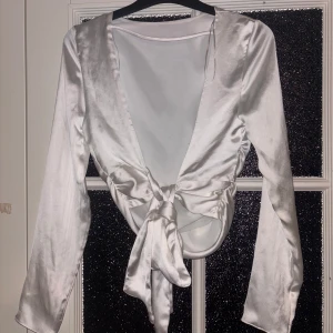 Siden långärmad från Zara - Snygg vit siden topp från Zara i ett glansigt material. Toppen har långa ärmar och en knytning där bak som ger en öppen rygg och elegant look. Perfekt för att klä upp en outfit!