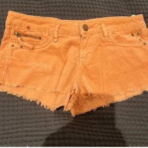 Orange manchester shorts - Snygga orange persiko färgade shorts i manchester med fransiga kanter och dekorativa nitar. Midja: 37cm längd: 20cm 💕 det passar inte mig så jag har ingen bild med dem på