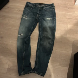  jeans med slitningar - Säljer ett par snygga  jeans från  jack and Jones  med slitningar för en cool look. Modellen är Tapered Mike. Storlek 31:32. Knappt använda 