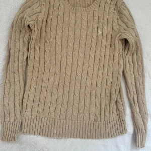 Beige stickad tröja från Polo Ralph Lauren - Säljer en superfin beige stickad tröja från Polo Ralph Lauren. Den har ett klassiskt flätmönster och är i storlek XS. Perfekt för höst och vinter med sina långa ärmar och mjuka material. Tröjan är i bra skick och redo för nya äventyr! 🍂✨