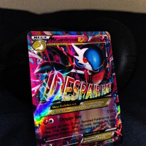 Pokémonkort Mega Gardevoir EX - Säljer ett coolt Pokémonkort av Mega Gardevoir EX. Kortet har en färgglad och glittrig design med texten 'Despair Ray'. Perfekt för samlare eller Pokémon-fans!                                                          
