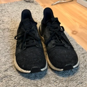 Svarta Adidas sneakers - Säljer ett par svarta Adidas sneakers med snörning och rund tå. Skorna har en bekväm sula och är perfekta för träning eller vardagsbruk. De är tillverkade i syntetmaterial och har en stilren design.