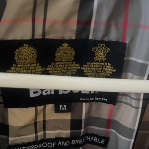 Gul vindjacka från Barbour - Säljer en stilren, oanvänd,  gul vindjacka från Barbour. Jackan har en dragkedja framtill och ett klassiskt rutigt mönster på insidan. Perfekt för blåsiga dagar med sin vattentäta och andningsbara design. Säljes i samband med för liten storlek. Ordinarie pris: 799. Mitt pris: 399