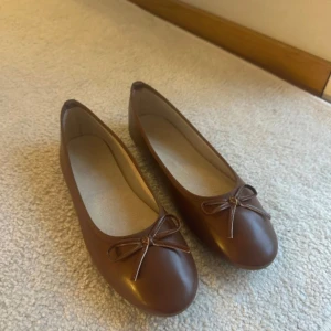 Bruna ballerinaskor - Snygga bruna ballerinaskor i syntetmaterial med en söt rosett på ovansidan. Perfekta för en stilren och bekväm look. Aldrig använda då de var lite för stora för mig! Köpte i en skobutik för 399.