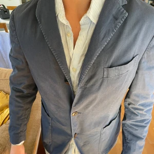 Blå kavaj från Boglioli - Snygg blå kavaj från Boglioli med klassisk design. Kavajen har en enkelknäppt front med tre knappar och flera fickor. Den är tillverkad i ett lätt material som ger en bekväm passform. Perfekt för en stilren look.(PRIS KAN DISKUTERAS VID SNABB AFFÄR)