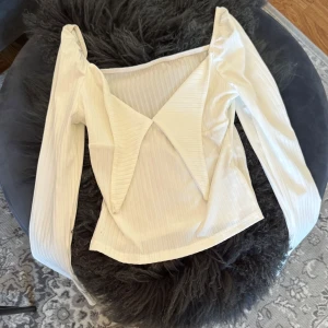 Vit ribbad blus - Säljer en stilren vit ribbad blus med långa ärmar och en unik design framtill. Perfekt för att lyfta vilken outfit som helst. Passar både till jeans och kjol.