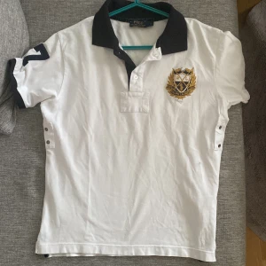 Vit kortärmad pikétröja från Ralph Lauren - Säljer en klassisk vit pikétröja från Ralph Lauren med broderad logotyp på bröstet. Tröjan har en mörkblå krage och knappar framtill. Perfekt för en stilren look! Stl S. Frakt tillkommer. 
