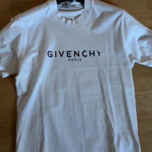 Vit t-shirt från Givenchy - Säljer en stilren vit t-shirt från Givenchy med deras ikoniska logga tryckt i svart på bröstet. T-shirten har en klassisk rund hals och korta ärmar. Perfekt för en minimalistisk look.
