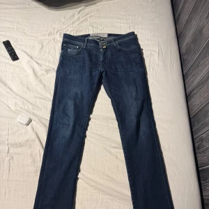Blå Jacob Cohen jeans - Snygga blå jeansbyxor med broderad text på insidan. De har en klassisk femficksdesign och knappar i gylfen. Perfekta för en avslappnad stil. Skick8,5/10 pågrund av liten slitning vid gylfen. Storlek 32.     Priset går att diskutera 