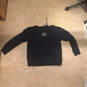 Blå sweatshirt - Säljer en stilren svart sweatshirt från HM med tryck på bröstet och text på ryggen. Tröjan har långa ärmar och en klassisk rund halsringning. Perfekt för en avslappnad look.