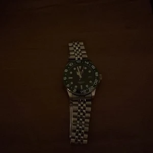 Kompass klocka - Snygg klocka med silverfärgad länk och svart urtavla. Tydliga markeringar och visare gör den lättläst. Perfekt för den som gillar stilrena accessoarer.