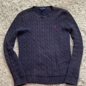 Mörkblå stickad tröja från Ralph Lauren - Säljer en stilren mörkblå stickad tröja från Ralph Lauren med kabelstickat mönster. Tröjan är andvänd fåtal gånger och är nästan nyskick. 