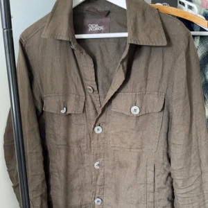 Mörkgrön  Oscar Jacobsonovershirt - Säljer en stilren  overshirt från Oscar Jacobson. Snygg mörkgrön khaki färg, bra skick, knappen på en ficka är lite trasig en lätt fix! Hör av er vid fler frågor