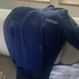 Mörkblå hoodie från Peak Performance - Säljer en snygg mörkblå hoodie från Peak Performance. Den har en dragkedja framtill och är perfekt för kyliga dagar. Klassisk design med logotyp på bröstet. Perfekt för både vardag och träning.