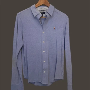 Ralph Lauren - Snygg blå långärmad skjorta från Polo Ralph Lauren med klassisk krage och knappar framtill. Den har en broderad logotyp på bröstet som ger en stilren touch. Perfekt för en stilmedveten look.