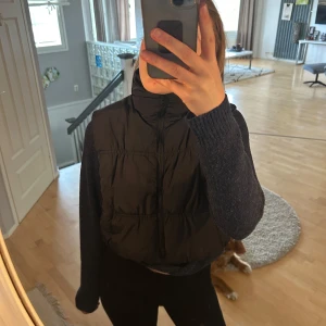 Svart dunväst  - Säljer en svart dunväst från HM. Västen har en dragkedja framtill och en hög krage för extra värme. Perfekt för lager-på-lager under kyligare dagar. Enkel och stilren design som passar till det mesta.