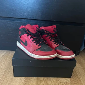 Nike Air Jordan Mid i rött och svart - Säljer ett par Nike Air Jordan Mid i rött och svart. Skorna har en klassisk design med snörning och rund tå. Perfekta för dig som älskar sneakers med stil och komfort. Gör rent skorna innan dom skickas!