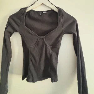 Grå ribbad topp från H&M - Snygg grå ribbad topp  lång ärm och en unik skärning vid bysten. Perfekt för en stilren look. Passar bra till både jeans och kjol.