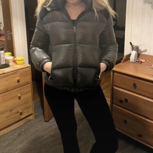 Svart dunjacka från Moncler - Säljer en snygg svart dunjacka från Moncler. Jackan har en pufferdesign med dragkedja och en stor logga på ryggen. Den är perfekt för kyliga dagar och har en huva för extra värme. Jackan är använd några gånger men jag har inte användning för den längre💕