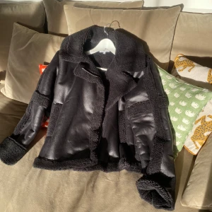 Svart jacka från NA-KD - Snygg svart jacka från NA-KD med mjuk teddy innuti och detaljer i teddy. Jackan har en klassisk krage och långa ärmar.  Den är lite i overzised fit