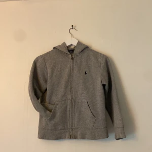 Grå hoodie från Polo Ralph Lauren - Säljer en stilren grå hoodie från Polo Ralph Lauren med dragkedja och broderad logga på bröstet. Perfekt för en avslappnad look. Den har en praktisk huva och fickor framtill. Pris kan ändras vid snabb affär.🔥🔥👍
