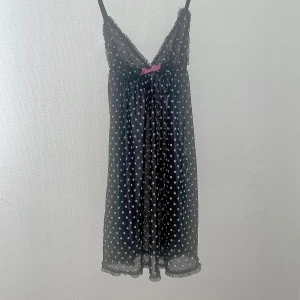 Svart prickig klänning från H&M - Söt svart klänning med vita prickar från H&M. Den har en v-ringad design med en rosa rosett framtill och smala axelband. STORLEK M (38) men passar även S (36).