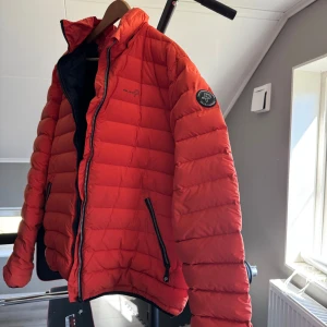 Orange pufferjacka från Pelle P - Säljer en snygg orange pufferjacka från Pelle P. Jackan har en dragkedja framtill och två praktiska fickor med dragkedjor. Perfekt för kyligare dagar med sin quiltade design.