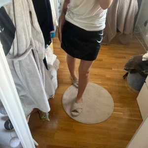 Svart kortkjol - Säljer en stilren svart kortkjol som passar perfekt till olika tillfällen. Kjolen har en enkel och elegant design som gör den lätt att matcha med olika toppar och accessoarer.