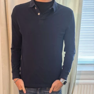 Peir One långärmad pikétröja - Snygg mörkblå pikétröja med långa ärmar och klassisk krage. Perfekt för en stilren look. Tröjan har knappar vid halsen för en justerbar passform.