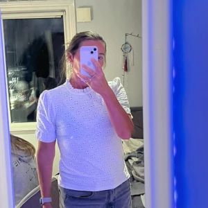 Vit blus med spetsdetaljer - Knapp back i halsen, normal i storleken jag är 169 cm lång! Säljer en söt vit blus med spetsdetaljer och korta ärmar. Blusen har en hög krage och ett vackert broderat mönster. Perfekt för en stilren look.