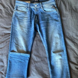 Blå jeans från Replay - Snygga blå jeans från Replay med klassisk femficksdesign och knappgylf. De har en bekväm passform och är perfekta för en avslappnad stil. Märket Replay är synligt på baksidan av midjan.
