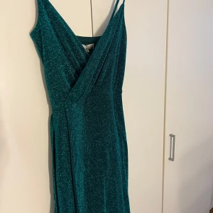 Glittrig grön balklänning - En glittrig grön balklänning ifrån Bubbleroom i helt nyskick! Lappen sitter kvar och är nyköpt för 1099kr. Storleken är 6UK vilket motsvarar en storlek XS-S, men materialet är ganska stretchigt. Som ni ser på en av bilderna så tillkommer det även ett resorband, där man kan knyta vid magen om man vill annars är det enkelt att ta av bandet också! Används inte tyvärr och därför är det bättre om den kommer till användning någon annan stans! 