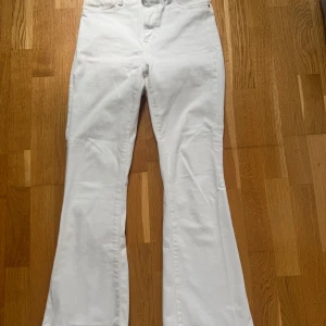 Vita bootcut jeans - Säljer ett par vita bootcut jeans med hög midja. Byxorna har klassisk femficksdesign och stängs med dragkedja och knapp. Perfekta för dig som vill ha en fräsch och stilren look. Har en pytteliten svag fläck på baksida ben men det är inget man lägger märke till.