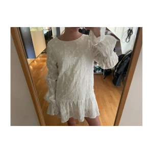 Vit blommig klänning med volang från NA-KD - Superfin vit klänning från NA-KD med blommigt mönster, volangkant nertill och långa ärmar. Klänningen har öppen rygg med knytband och är perfekt till sommaren!Passar perfekt som studentklänning🌸jag är 168