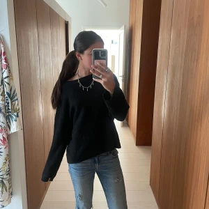 Svart stickad tröja - En svart stickad tröja med lång ärm och avslappnad passform. Tröjan har en enkel design utan synliga detaljer och passar perfekt till jeans. Mjuk och skön för kyligare dagar.