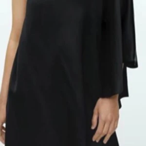 Boxy Minidress  - Elegant svart långklänning från By Malene Birger i oneshoulder-modell. Klänningen har en lös passform och är tillverkad i ett glansigt, mjukt material som ger en lyxig känsla. Perfekt för dig som vill sticka ut med en stilren och modern look. Helt ny 