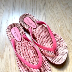 Rosa flip-flops från ILISE JACOBSEN - Säljer ett par rosa flip-flops från ILISE JACOBSEN med flätad sula och klassiska remmar. Perfekta för varma dagar och strandhäng. Superlätta och bekväma att ha på sig. 