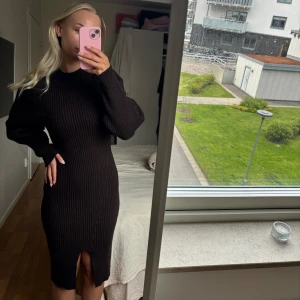 Brun ribbad stickad långklänning - Säljer en brun stickad långklänning med ribbad struktur och lång ärm. Klänningen har en tight passform och en liten slits framtill. Perfekt för dig som gillar stilrena och enkla plagg med en twist.