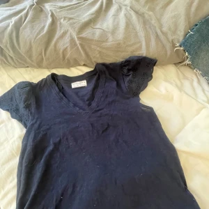 Mörkblå topp med spetsdetaljer från Holly & Whyte - Säljer en mörkblå topp från Holly & Whyte med v-ringning och korta ärmar med fina spetsdetaljer. Perfekt till sommaren och enkel att matcha med jeans eller kjol. Vill bli av med den! Passar även s💖