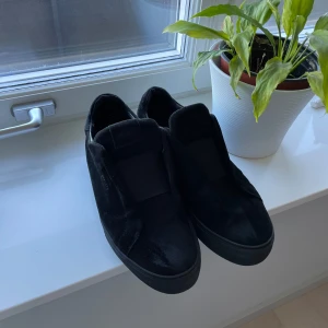 Axel Arigato skor  - Säljer ett par stilrena svarta sneakers från Axel Arigato. De är i mocka och har en enkel design utan snörning. 