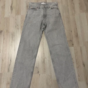 Grå jeansbyxor från Gina Tricot - Säljer ett par raka grå jeans från Gina Tricot. Klassisk femficksmodell med knapp och dragkedja i gylfen. Jeansen har en normal passform och är tillverkade i denim.